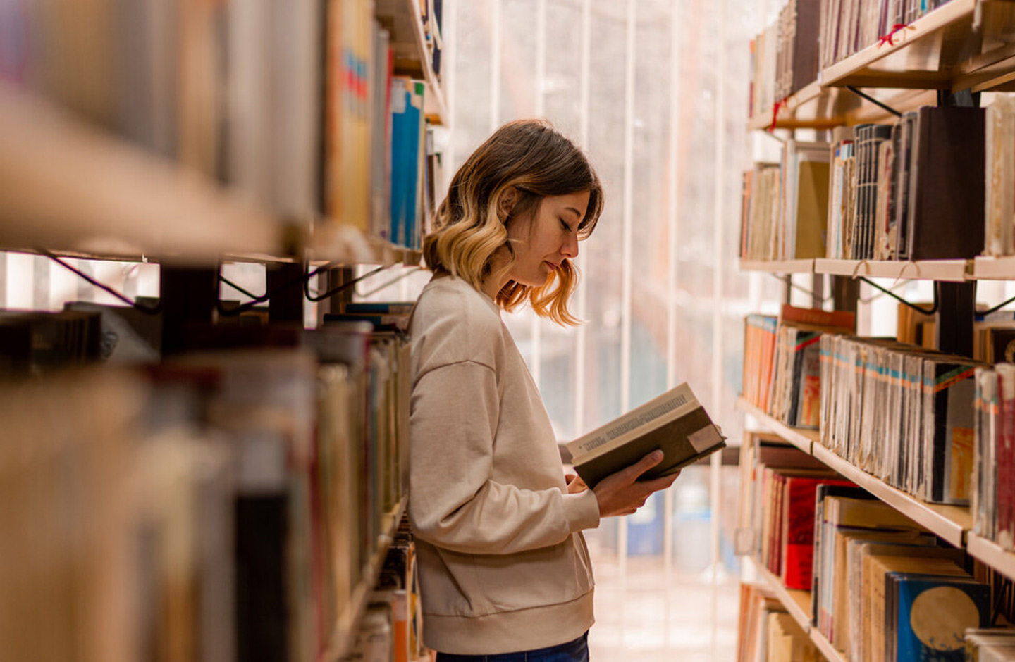 jovem mulher a ler um livro em corredor de biblioteca