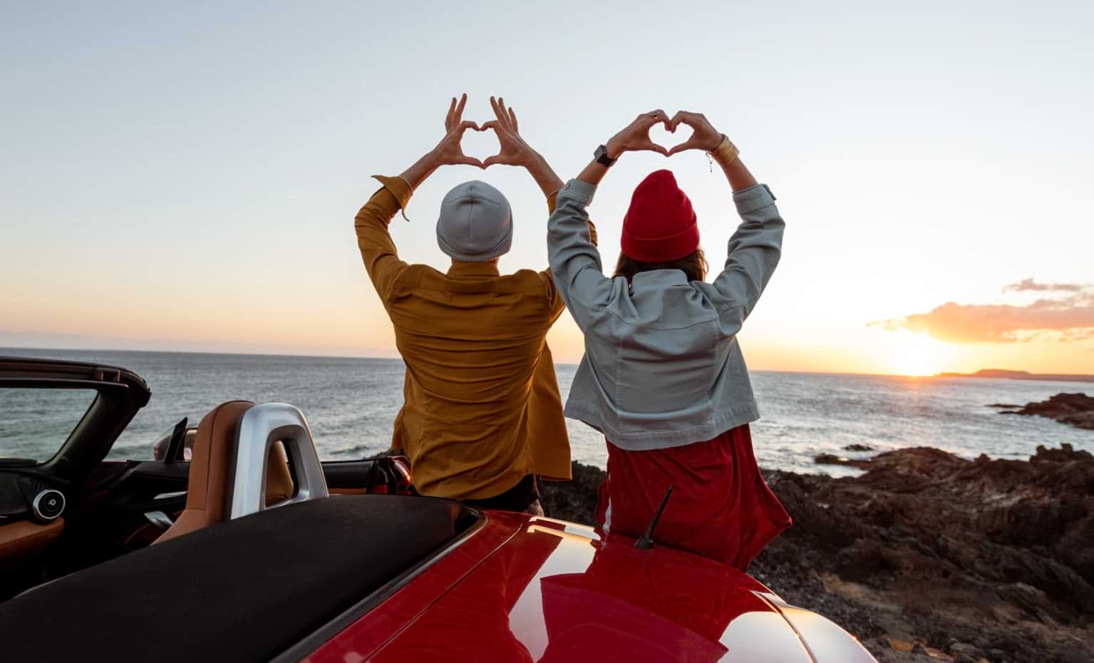 Duas pessoas fazem corações com as mãos a ver um pôr do sol