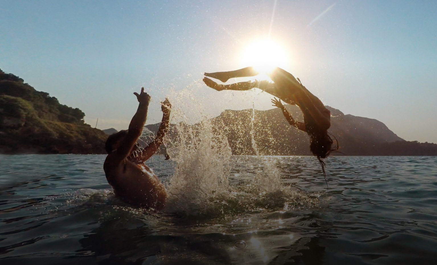 Duas pessoas fazem piruetas na água do mar