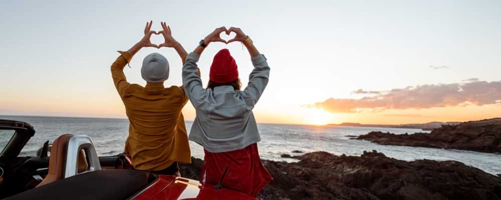 Duas pessoas fazem corações com as mãos a ver um pôr do sol
