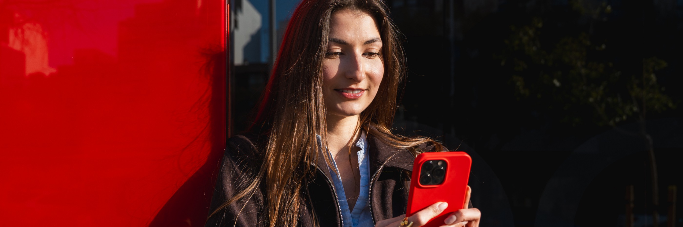 mulher jovem sorri com smartphone na mão porque tem Conta Jovem Santander