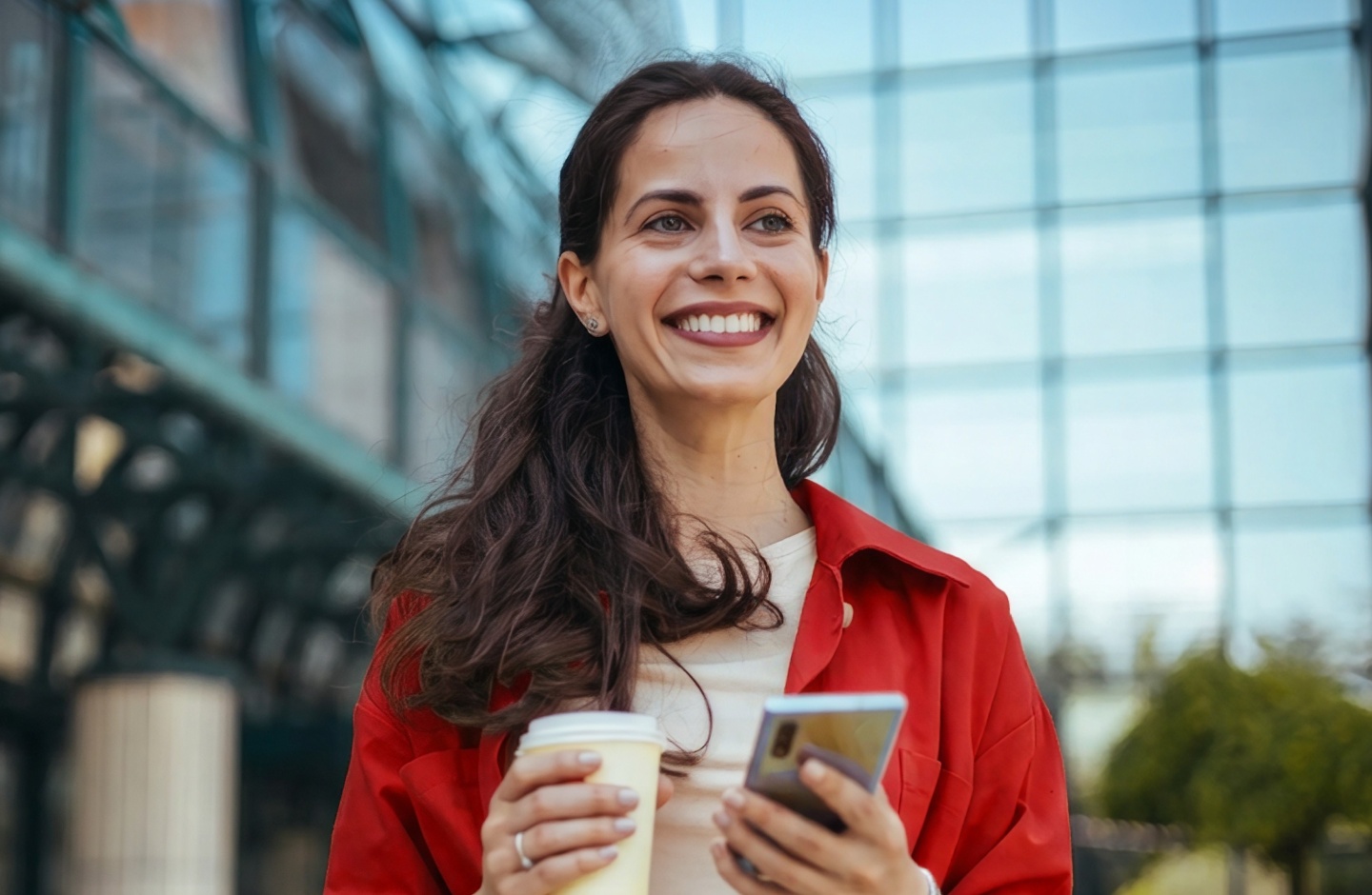Mulher sorri com smartphone e café na mão porque tem Conta Santander Mais