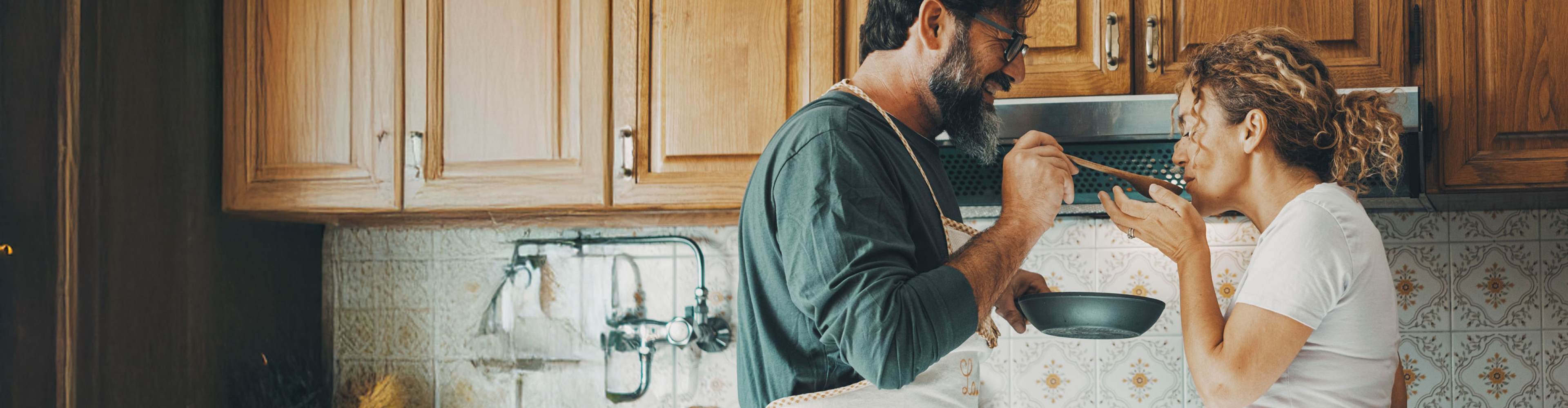 Casal na cozinha da sua habitação dão a provar comida um ao outro