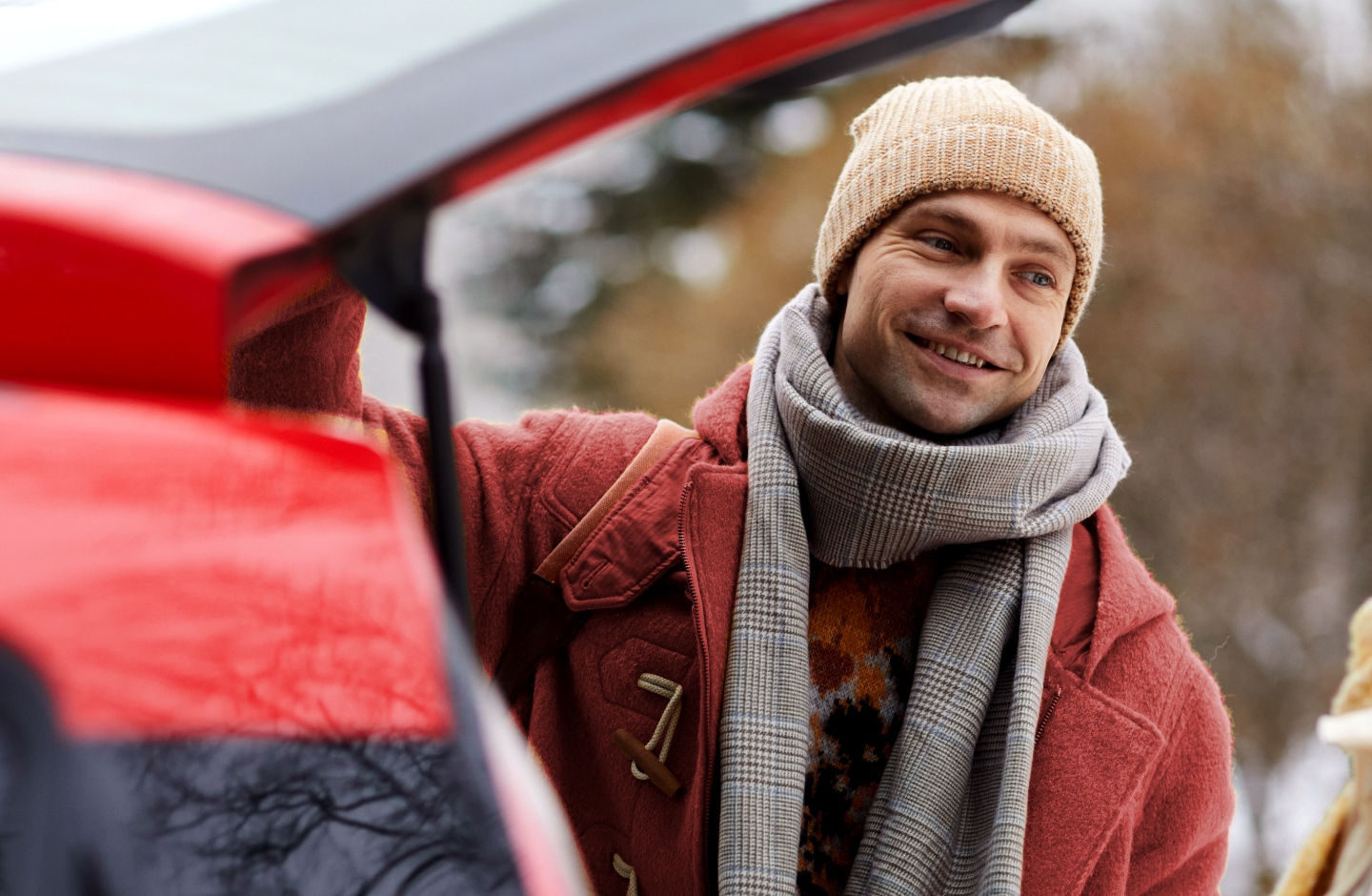 Homem sorridente, bem agasalhado, mexe na mala do carro