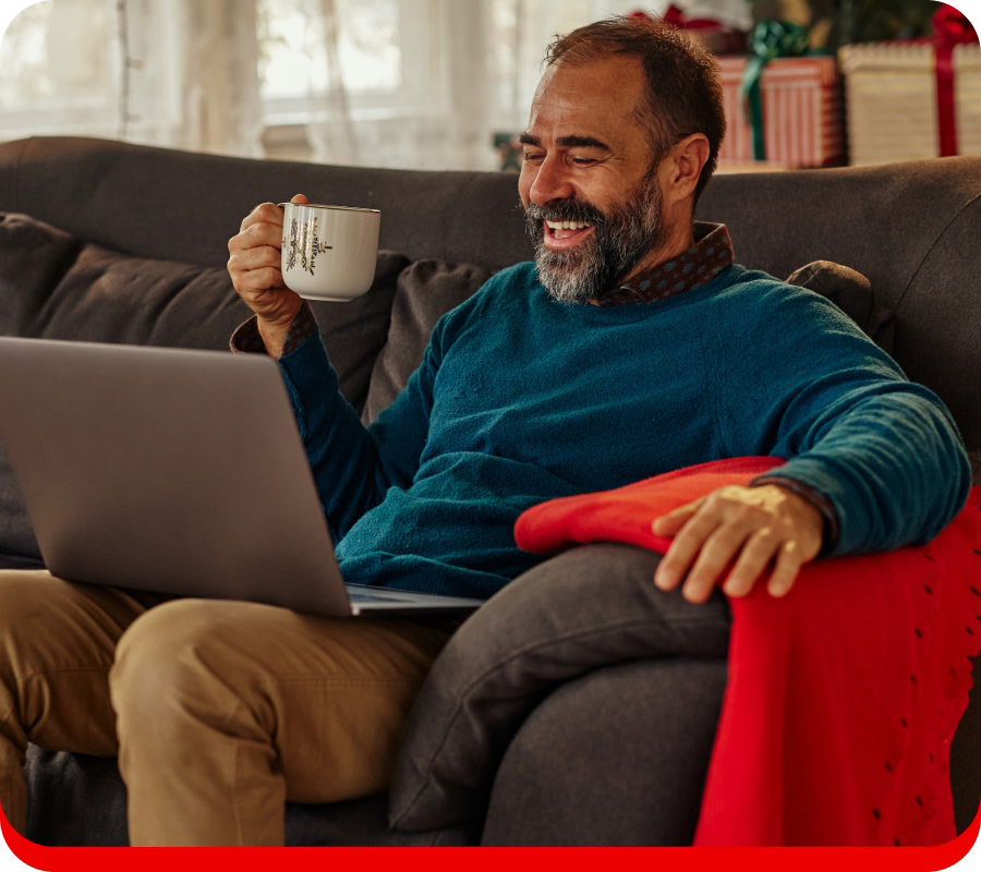 Homem relaxado no sofá com computador portátil e uma chávena na mão