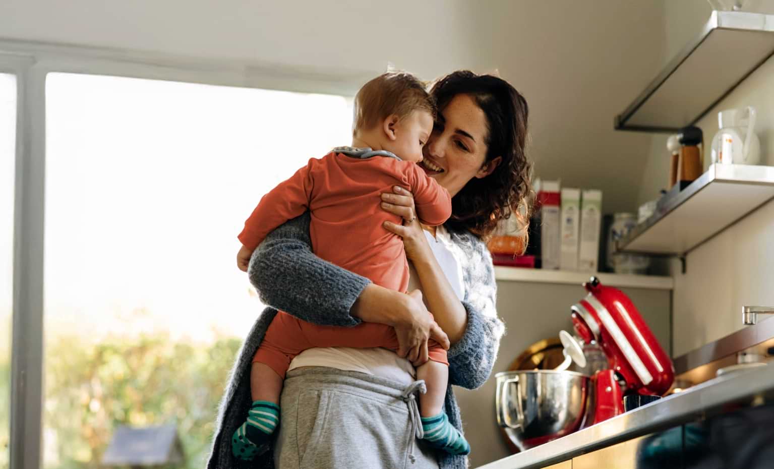 Mãe com criança ao colo na cozinha de casa