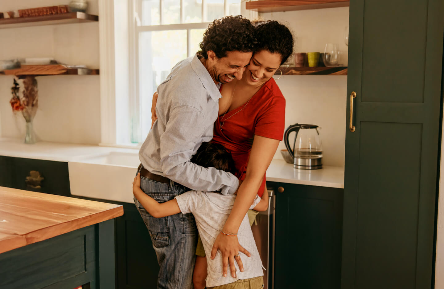 Casal de homem e mulher abraçam criança na cozinha
