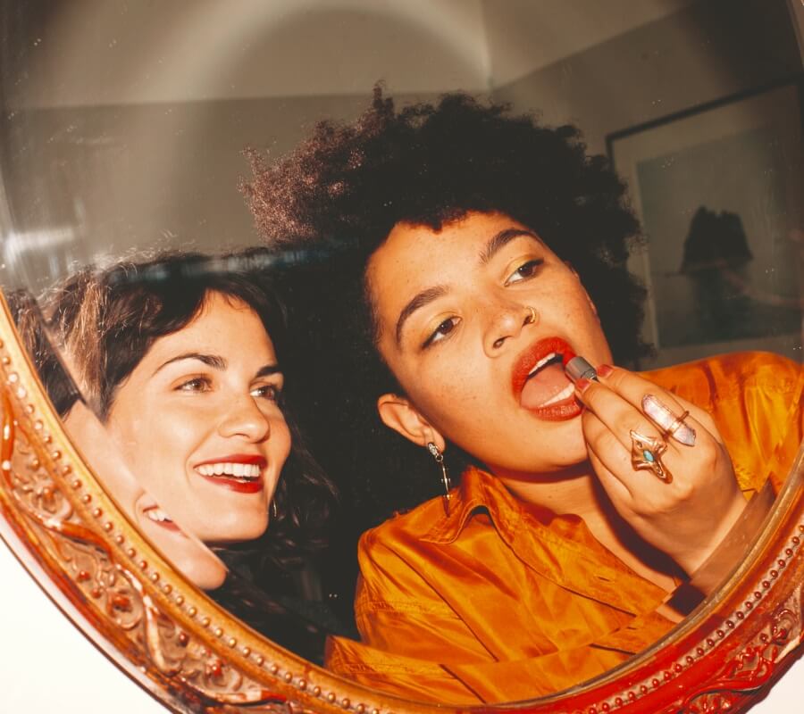 Duas amigas pintam os lábios em frente ao espelho