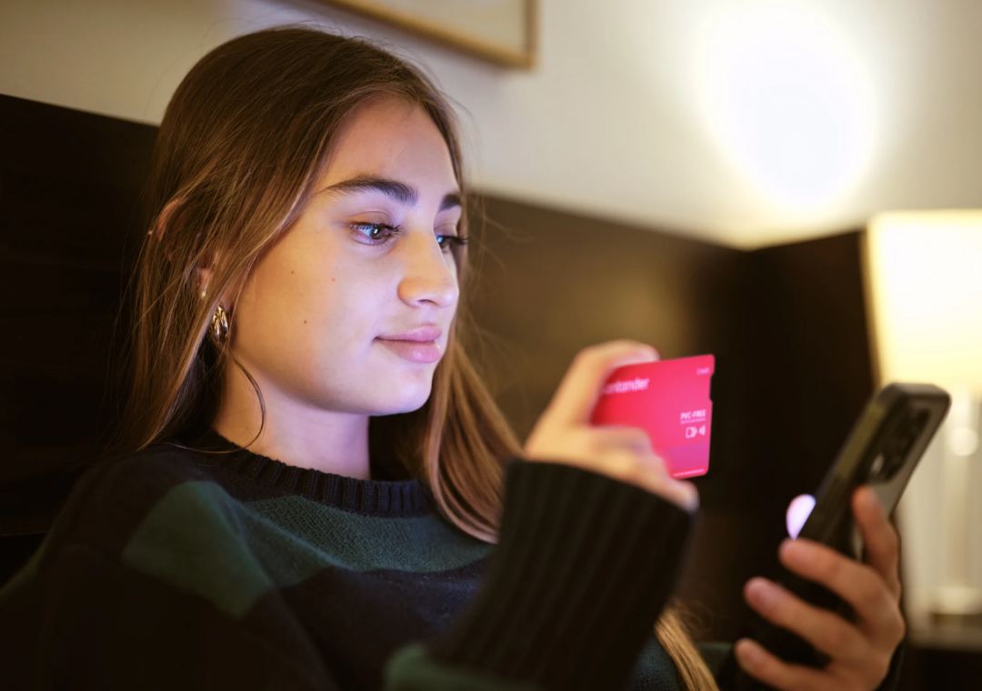 Mulher jovem com cartão Santander e smartphone na mão