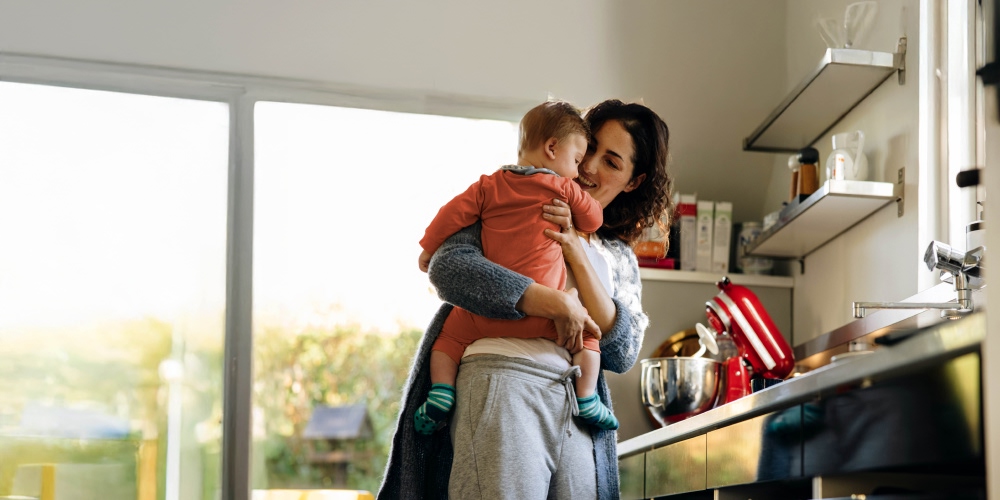 Mãe com criança ao colo na cozinha de casa
