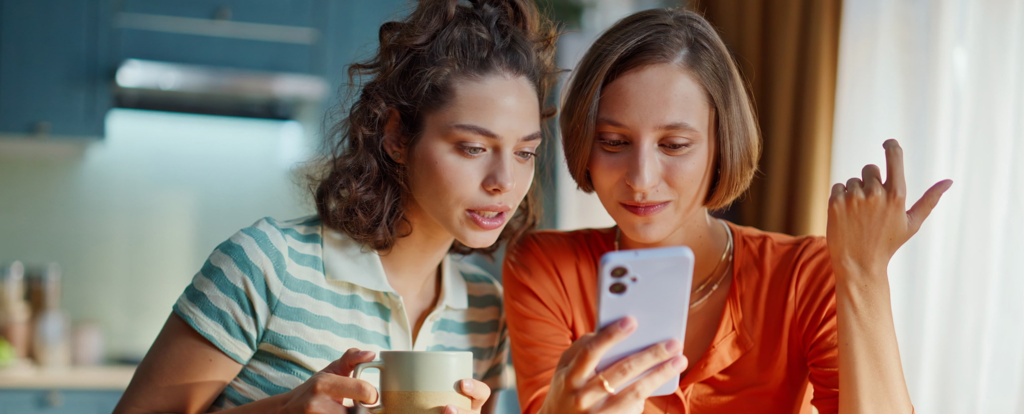 mulher partilha conteúdo no smartphone com outra mulher que tem chávena na mão
