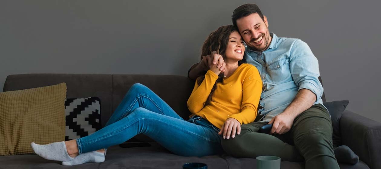 Casal de homem e mulher abraçados no sofá da casa com seguro