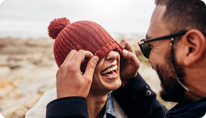 Casal de homem e mulher felizes na praia enquanto o homem puxa o gorro à mulher
