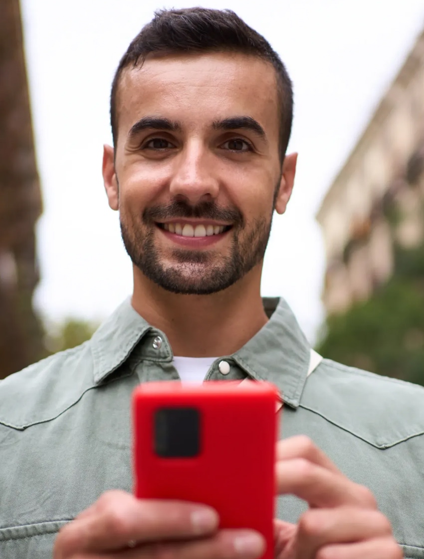 Homem sorri com smartphone na mão e olha em frente