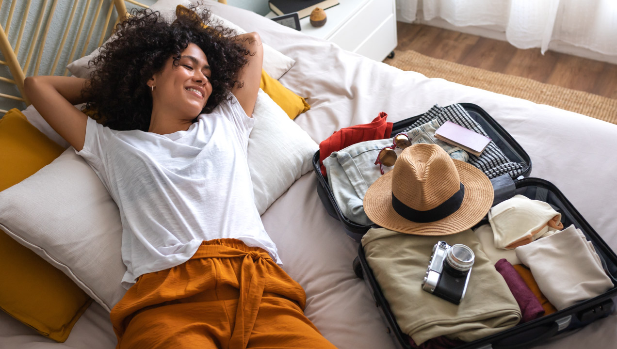 Senhora deitada na cama feliz ao lado da mala de viagem feita e aberta
