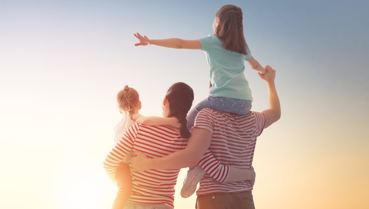 Família com dois pais e duas crianças felizes a ver o pôr do sol