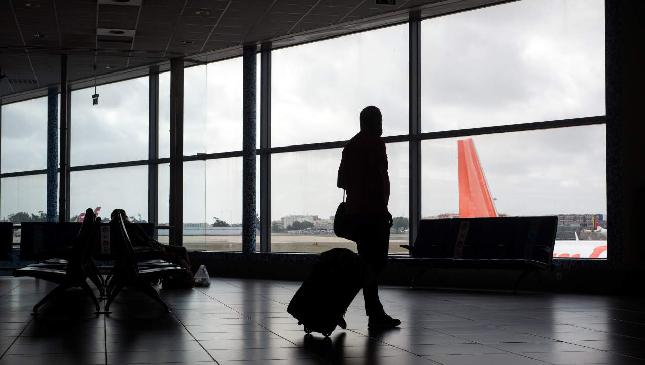 Silhueta de um passageiro com mala de viagem no aeroporto a olhar para um avião 