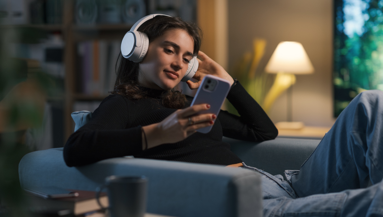 Mulher jovem sentada no sofá da sala com fones nos ouvidos a ouvir aulas de inglês