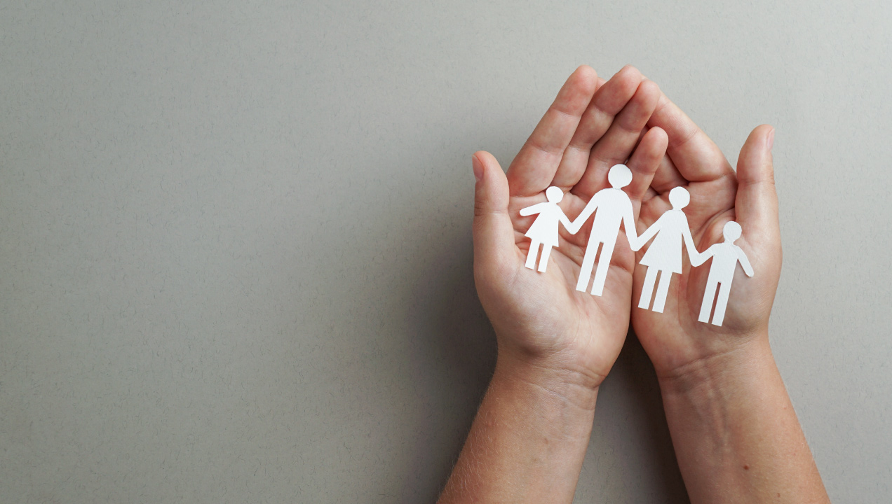Mãos juntas a segurar uma figura de papel de uma família dois pais e dois filhos