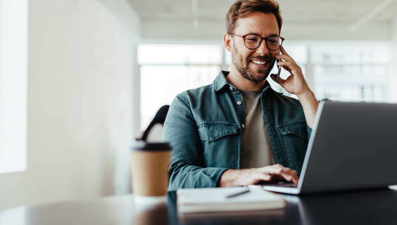 Empresário sentado a trabalhar no computador enquanto fala ao telemóvel sorridente