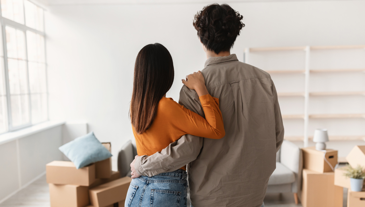 Casal abraçado numa casa com caixas de mudanças a observar o seu novo espaço