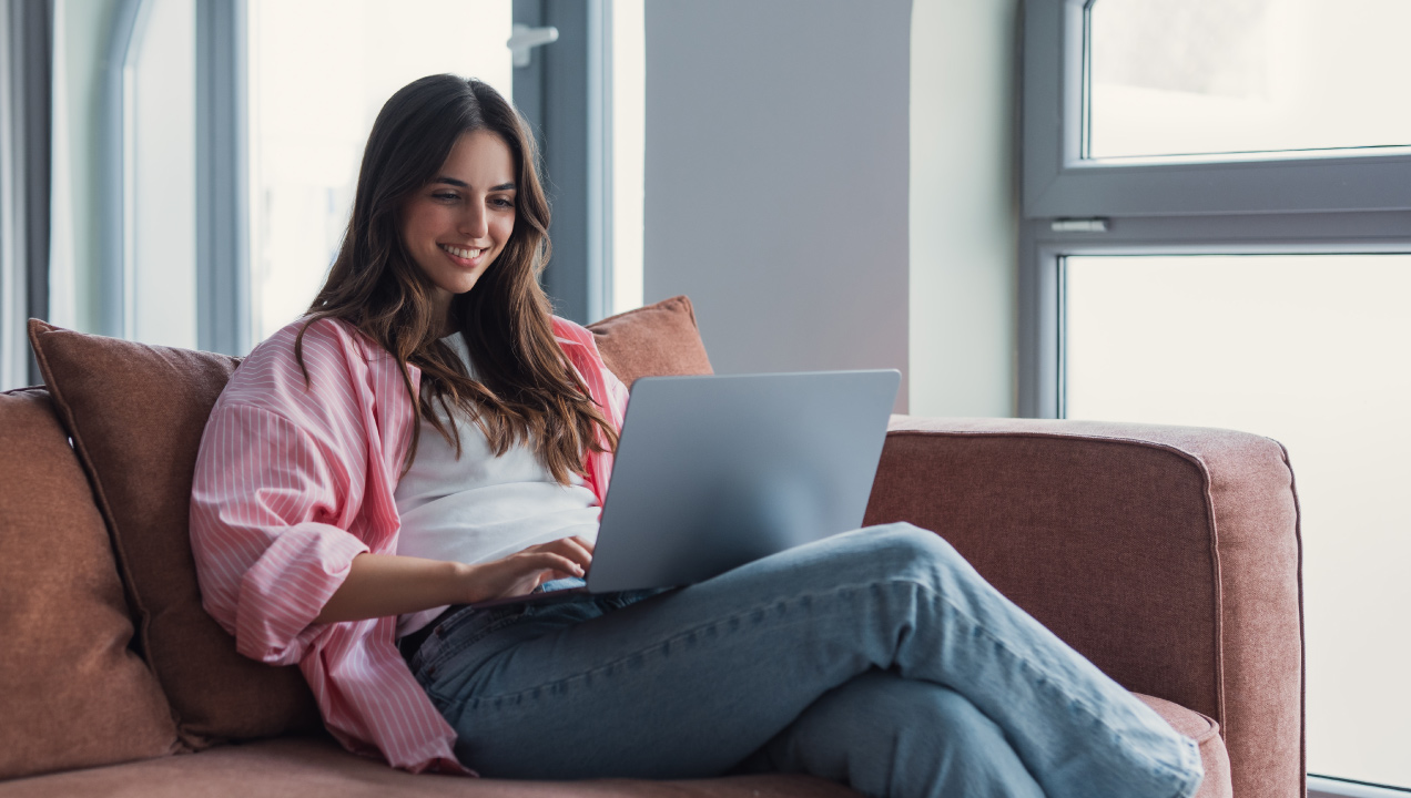 Rapariga jovem sentada no sofá sorridente enquanto mexe no computador