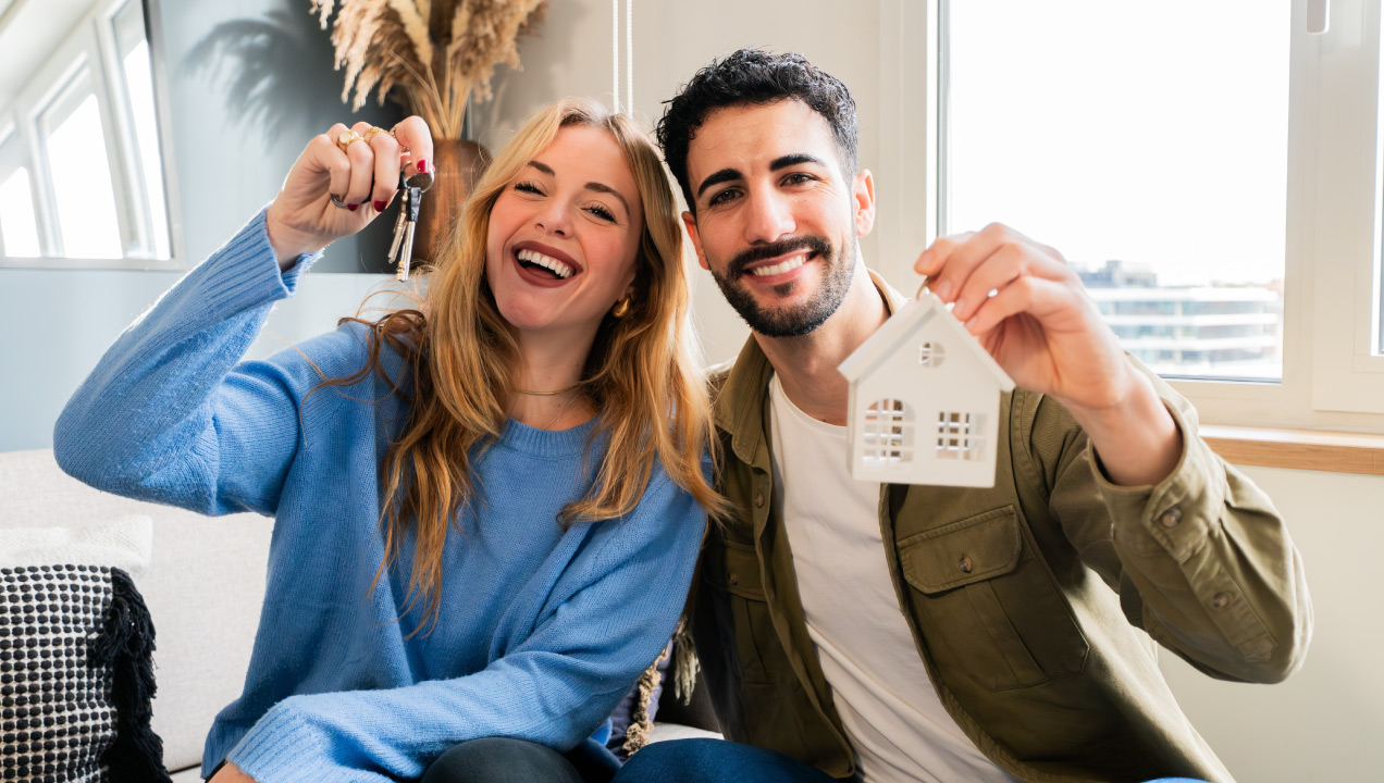 Casal feliz sentado na sala de casa e a segurar as chaves de casa 