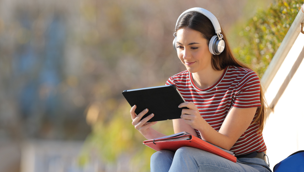 Jovem sentada num jardim a ouvir uma aula e a mexer no tablet