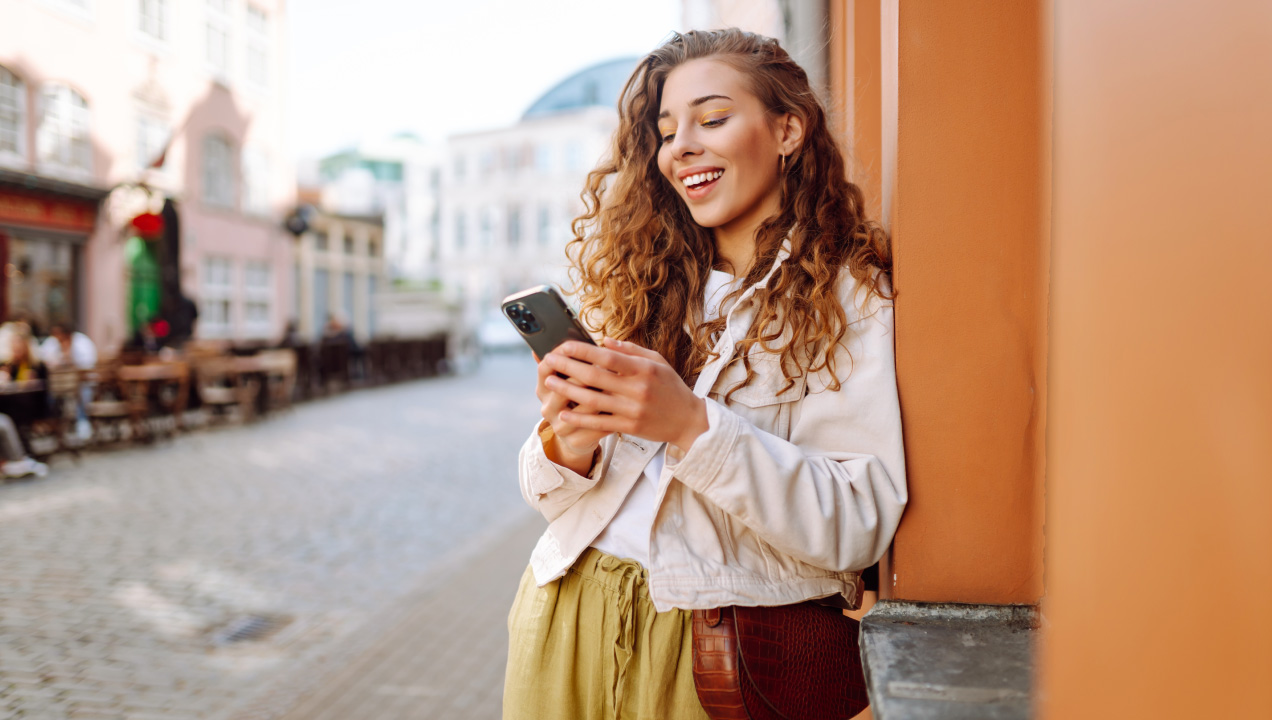 Mulher jovem a andar na rua feliz a mexer no telemóvel