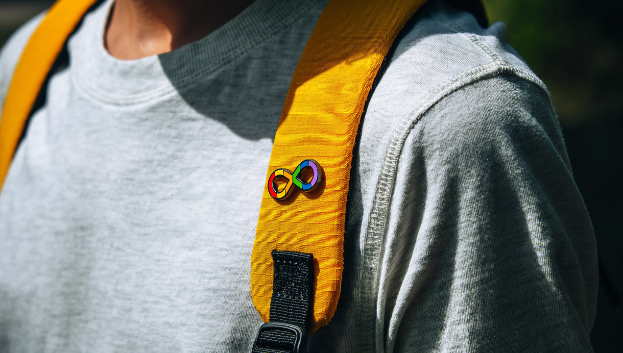 Rapaz com a mochila nas costas e um pin de um laço colorido na alça da mochila