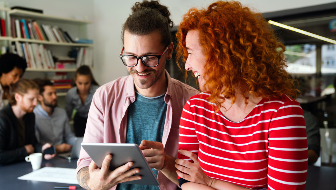 Dois profissionais a consultar informação num tablet num am biente de trabalho partilhado