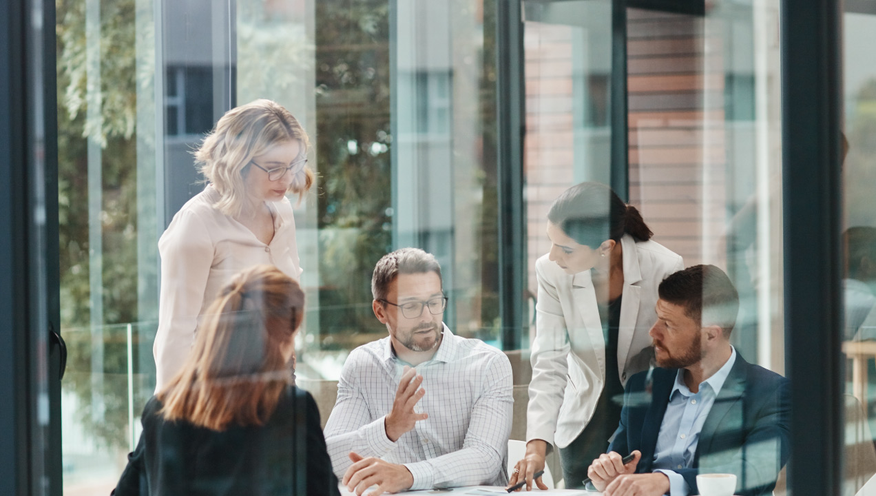Ambiente de escritório com 5 pessoas a conversarem à volta de uma mesa