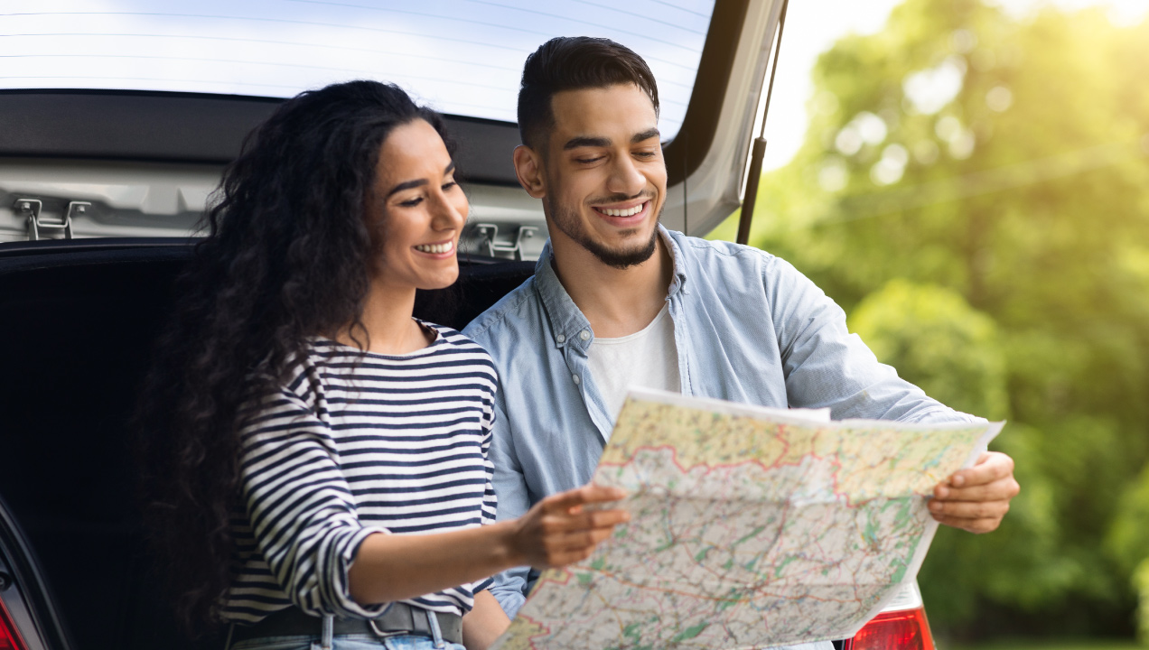 Casal feliz sentado na bagageira do carro a analisar um mapa 