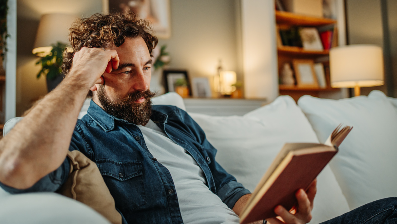Homem sentado no sofá a ler um livro num ambiente acolhedor