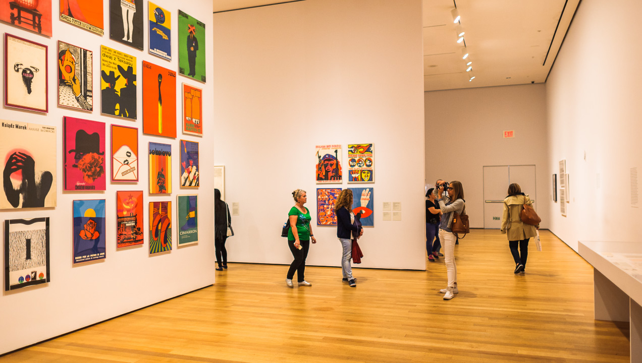 Várias pessoas a visitarem uma galeria de arte e a verem os quadros