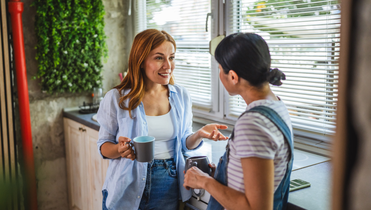 Duas colegas de trabalho a conversarem na copa enquanto bebem café