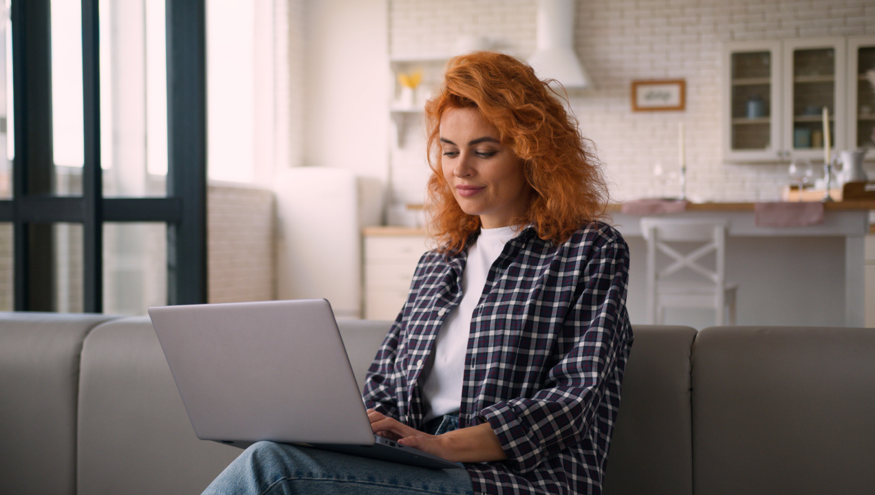 Senhora sentada no sofá de casa, a mexer no computador