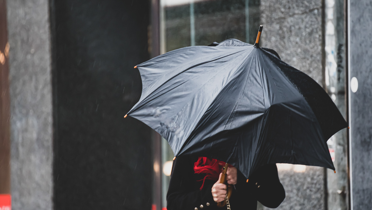 Pessoa a andar na rua com chuva e a proteger-se com chapéu