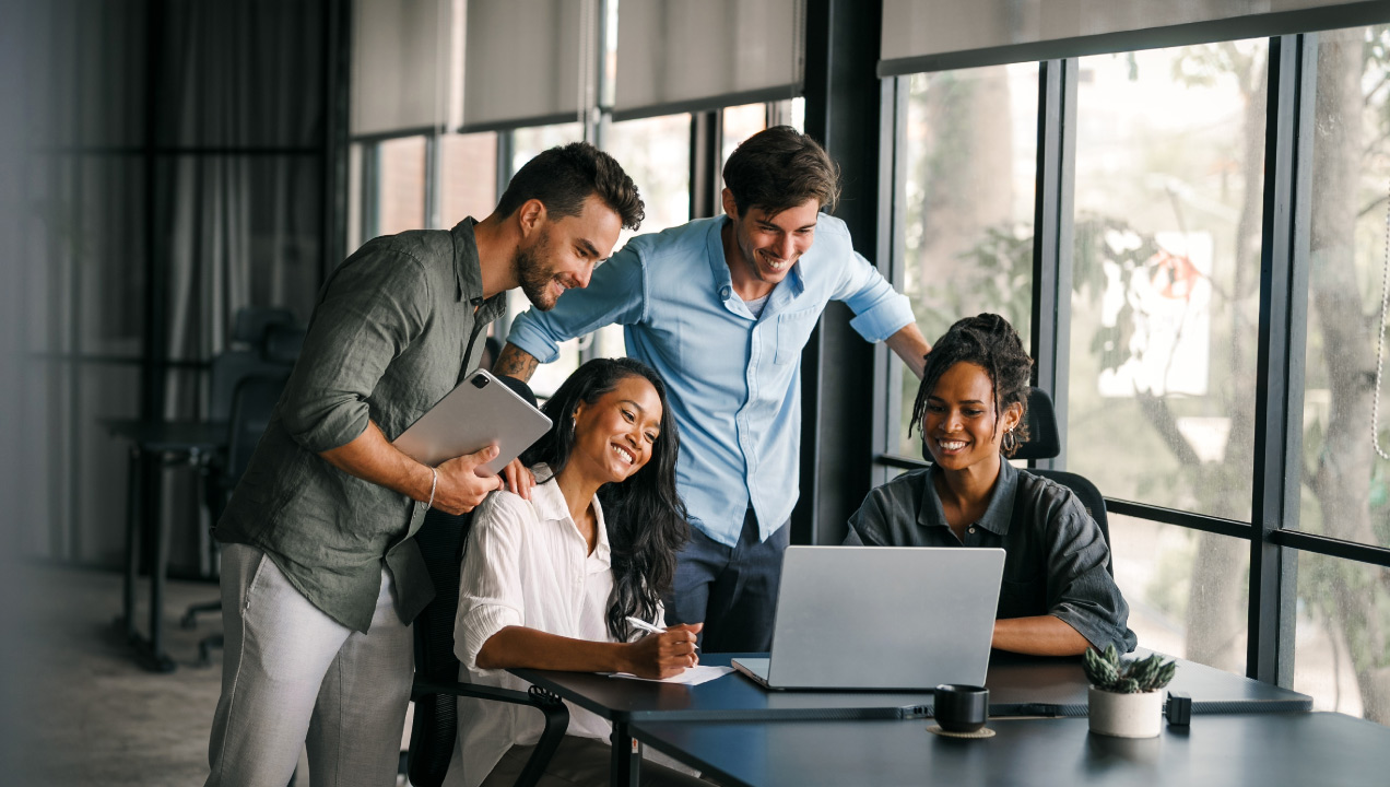 Colegas de trabalho reunidos no escritório felizes a ler notícia no computador