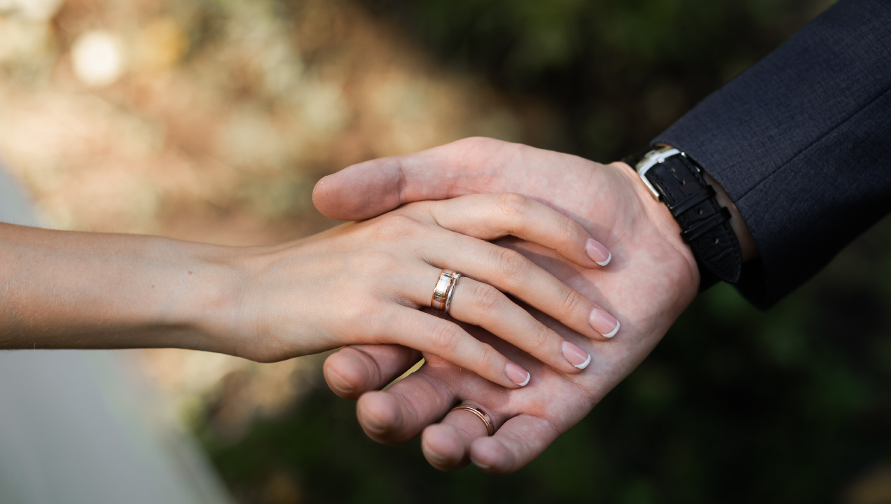 Mãos de casal dadas com alianças a simbolizar casamento