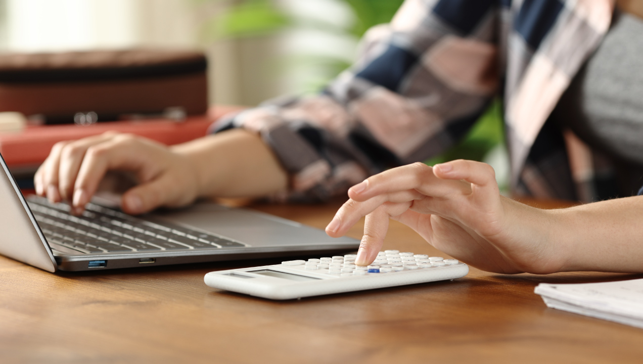 Senhora a mexer no computador e a fazer contas na calculadora