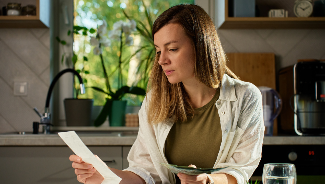 Senhora sentada na cozinha, a analisar faturas e dinheiro