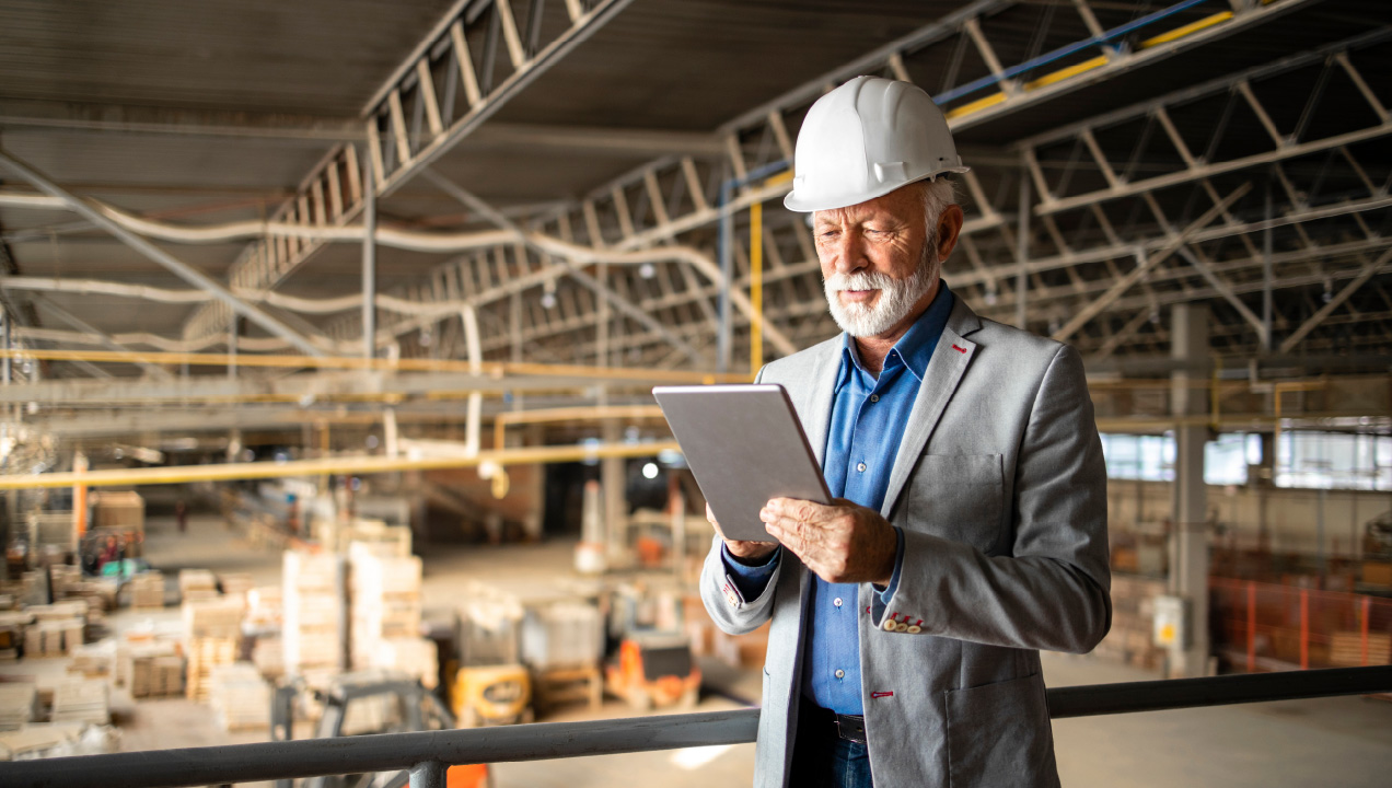 Senhor com capacete de obras, numa fábrica a mexer num tablet