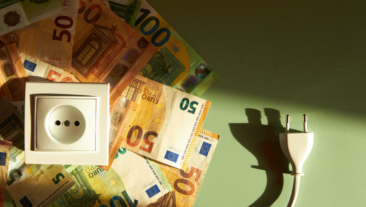 Várias notas de cinquenta euros e cem euros disposta ao lado de uma tomada elétrica