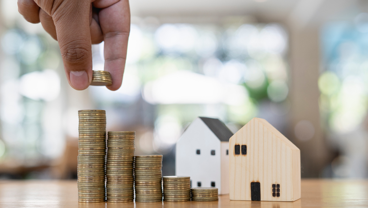 Casinhas de madeira numa mesa e alguém a colocar várias moedas numas espécies de torres