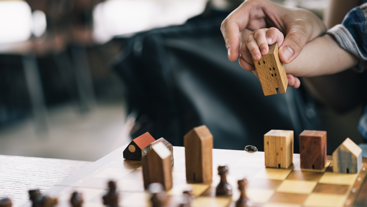 Adulto a segurar mão de criança num jogo de tabuleiros com peças de mandeira de casas