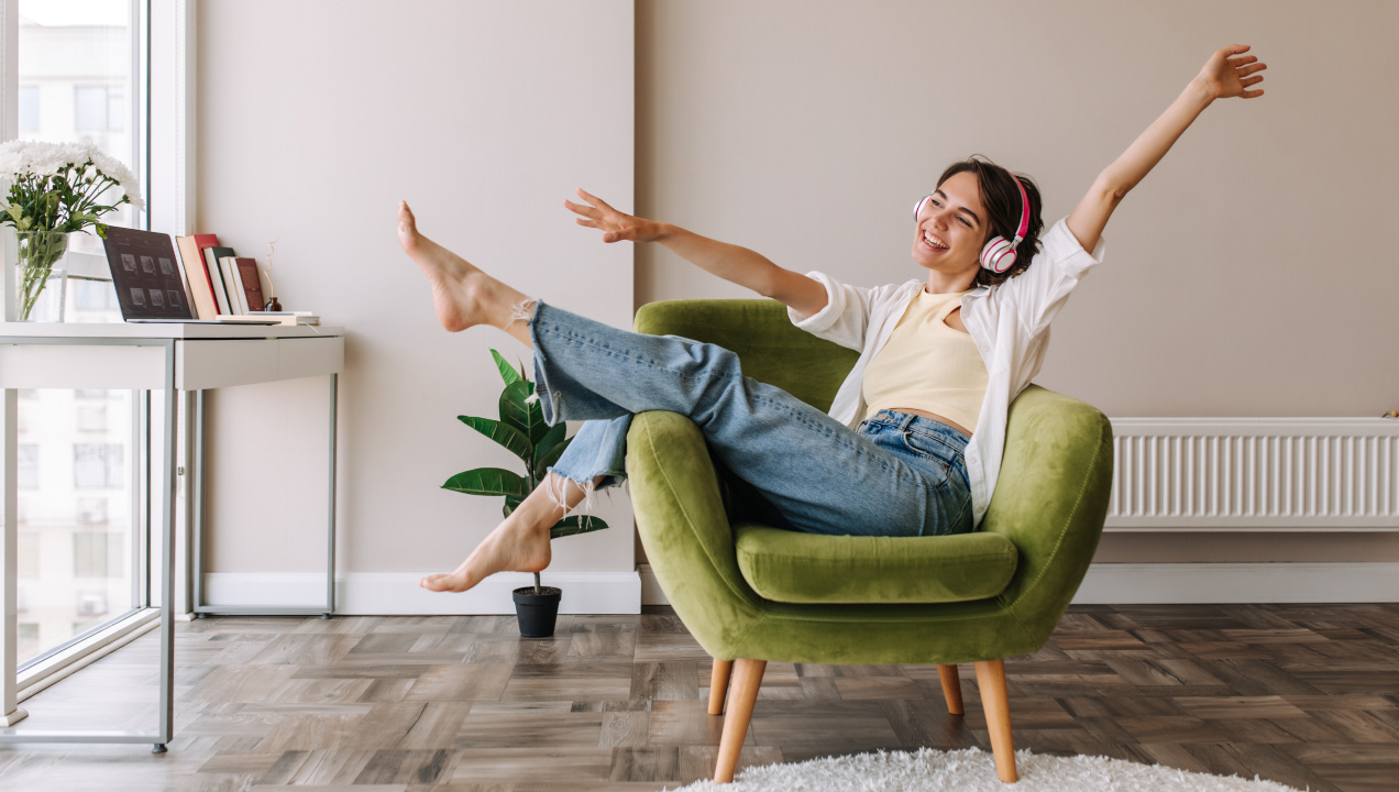 Mulher divertida ouve música com headphones num sofá poltrona
