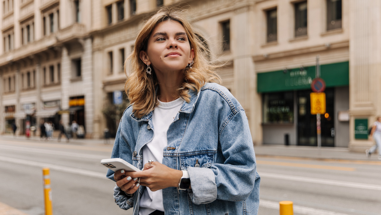 Senhora feliz a andar na rua e a mexer no telemóvel