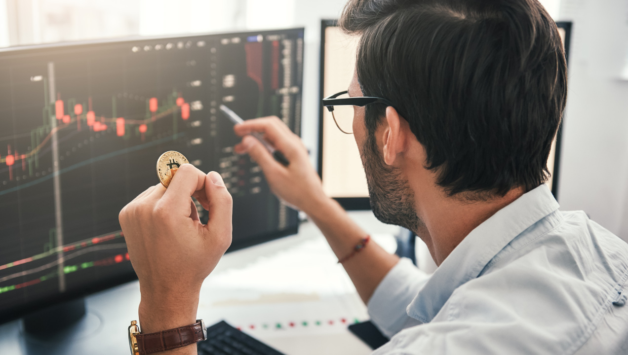 investidor segura uma moeda bitcoin e consulta ecrã com gráficos investidor segura uma moeda bitcoin e consulta ecrã com gráficos