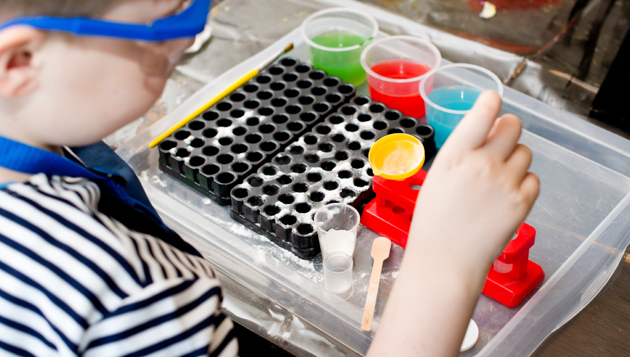 Criança com um tabuleiro com objetos para fazer uma experiência